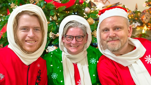 Tre julepyntede bibliotekarer i rødt og grønt (AI)