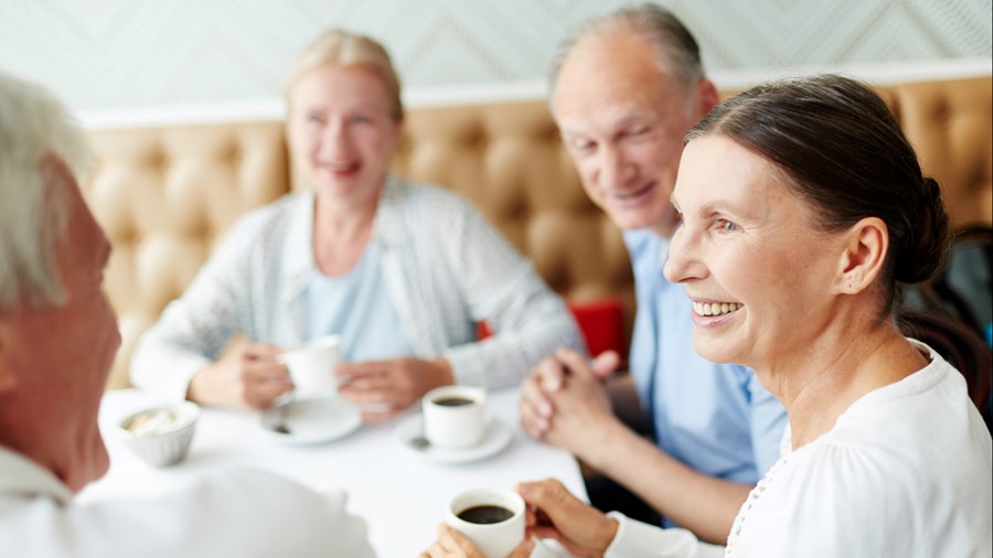 Gruppe voksne og eldre sitter ved et bord og drikker kaffe sammen