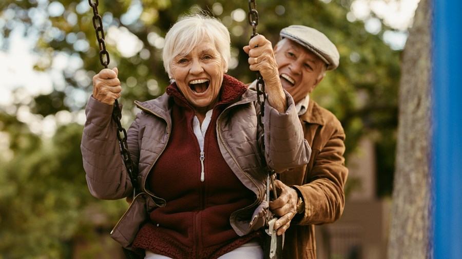 Senior man pushing his female partner on swing in park and having fun together. Playful and happy senior couple enjoying at swing in park .