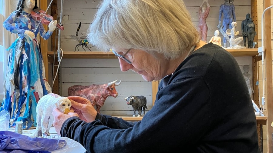 Bildet viser en kunstner som jobber med en dyreskulptur, bak henne ser vi andre skulpturer hun har laget.