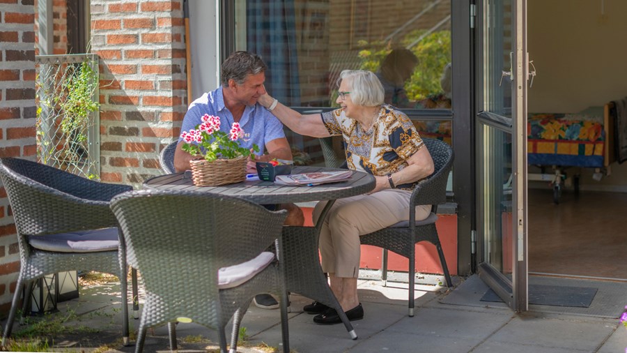 Eldre kvinne og voksen mann som sitter ved terrassebord