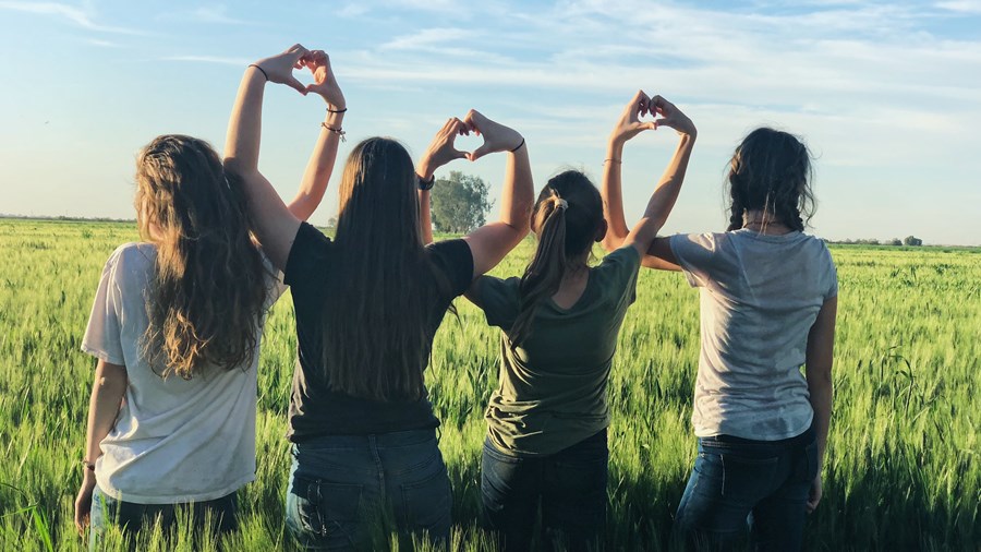 Fire jenter på en grønn slette som lager hjerter med hendene. 