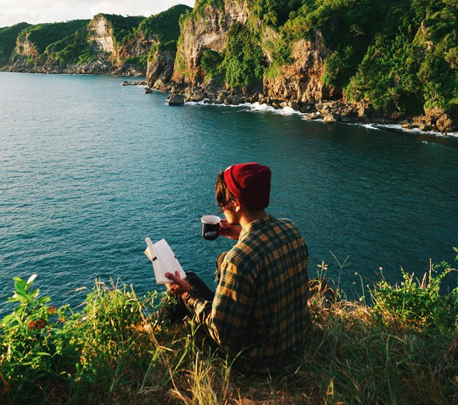 Person som leser bok med utsikt over havet