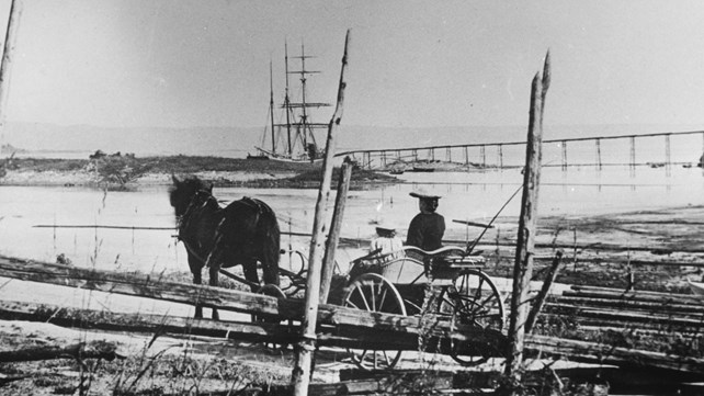 Gammelt bilde av hest med vogn og mennesker med båt i bakgrunnen